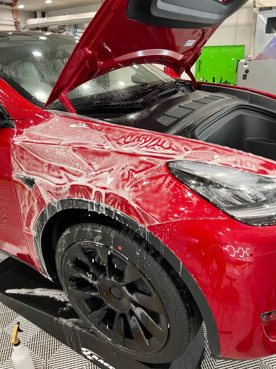 Paint protection film being wet-laid over the front end of a red Tesla Model Y