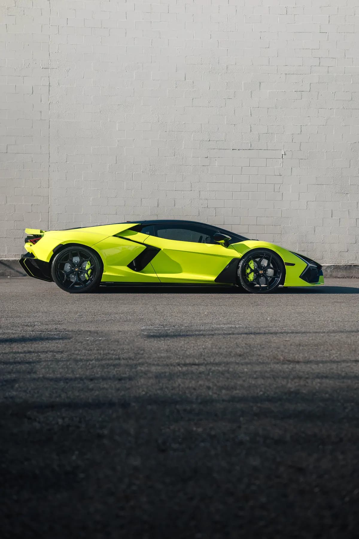 Side profile of a lime Lamborghini Revuelto against a white wall